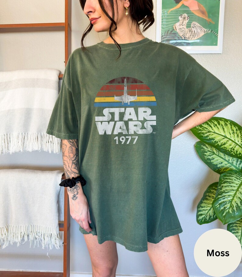 May include: A green oversized t-shirt with a vintage Star Wars graphic. The graphic features a sunset with a spaceship flying through it. The text "Star Wars 1977" is printed below the graphic.