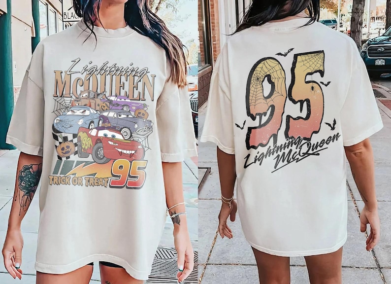 K&ouml;nnte beinhalten: Cremefarbenes Lightning McQueen Grafik-T-Shirt. Die Vorderseite zeigt ein Cartoon-Bild von Lightning McQueen und anderen Autos mit Halloween-Elementen. Auf der R&uuml;ckseite ist eine gro&szlig;e "95" mit Spinnennetz-Design und dem Text "Lightning McQueen" abgebildet.