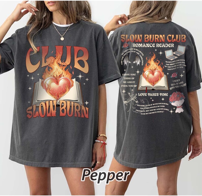 May include: Dark gray t-shirt with a front graphic featuring the text "CLUB SLOW BURN" above an open book with a flaming heart. The back of the shirt has additional text and graphics, including "SLOW BURN CLUB ROMANCE READER".
