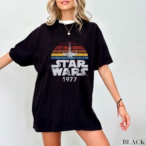 May include: Black t-shirt with a vintage Star Wars graphic featuring a spaceship and the text "Star Wars 1977".