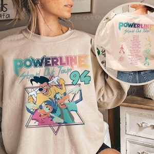 K&ouml;nnte beinhalten: Beiges Sweatshirt mit farbenfroher Grafik von Powerlines Stand Out Tour '94 mit Zeichentrickfiguren. Auf der R&uuml;ckseite des Sweatshirts befinden sich das Powerline-Logo und Tourdetails. Das Design beinhaltet ein Dreieck und die Zahl 94.
