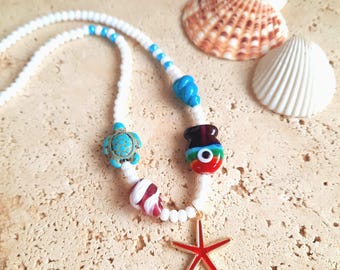 May include: A white beaded necklace with turquoise turtle and colorful glass bead charms, and a red starfish pendant. Two seashells are in the background. The necklace is a beach-themed accessory.