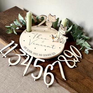 Può includere: Centrotavola di compleanno in legno con base circolare, con i nomi "Theo & Vincent" e la frase "Wie schön, dass ihr geboren seid." Include una volpe e un cervo ritagliati, due candele e numeri di legno 1-0.