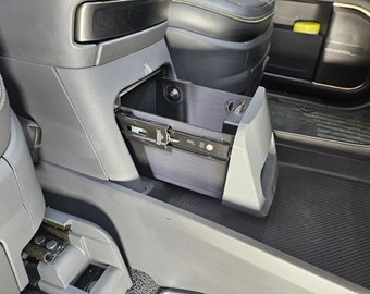 Op de afbeelding: Een grijs auto-interieur met een zwart plastic opbergvak dat eruit schuift. Het vak is open en leeg.