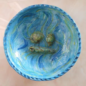 May include: A blue ceramic bowl with a wavy design and three seashells. The bowl is decorated with a blue and green glaze.