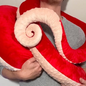 May include: A large, plush red and pink octopus pillow. The pillow is shaped like an octopus with a curled tentacle.