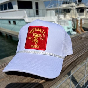 May include: White trucker hat with a red and gold Fireball Whisky patch. The patch features a dragon and the words "Red Hot Whisky".