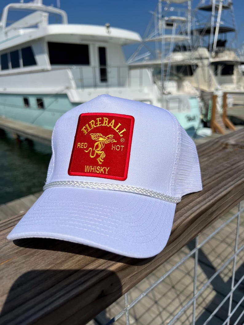 May include: White trucker hat with a red and gold Fireball Whisky patch. The patch features a dragon and the words "Red Hot Whisky".