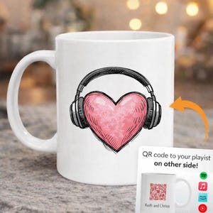 May include: White ceramic mug featuring a pink heart design with headphones. The heart is textured and the headphones are black. A small card with a QR code and the text "QR code to your playlist on other side!" is visible.