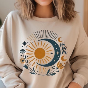 May include: A beige sweatshirt with a graphic print of a sun and moon with floral accents. The sun is yellow and the moon is blue.
