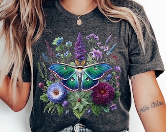 May include: A dark gray t-shirt with a colorful moth and floral design. The moth is green, blue, and purple with a white outline. The flowers are purple, blue, and pink.