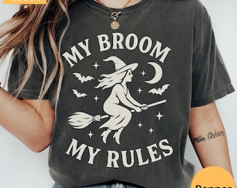May include: Dark gray t-shirt with the text "MY BROOM MY RULES" in white. The graphic features a witch on a broom, bats, stars, and a crescent moon. The shirt has a crew neck and short sleeves.