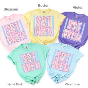 May include: Five short-sleeved crewneck t-shirts in pastel colors: Blossom pink, Butter yellow, Violet purple, Island Reef green, and Chambray blue. Each shirt features a central graphic with vertical blue stripes and the text SST CREW in pink.