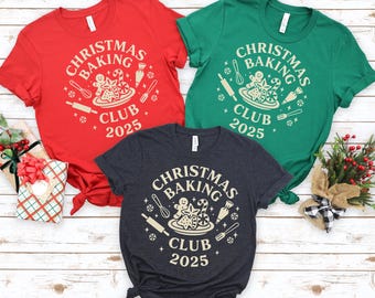 Könnte beinhalten: Drei kurzärmelige T-Shirts in Rot, Grün und Anthrazitgrau. Jedes Shirt zeigt ein rundes Design mit dem Text "CHRISTMAS BAKING CLUB 2025" und Backmotiven, darunter eine Teigrolle und Lebkuchenmännchen.