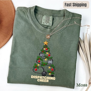 Op de afbeelding: Een mosgroen t-shirt met ronde hals en een afbeelding van een kerstboom gevormd door een zwart headset-snoer, versierd met rode kerstballen, gele lichtjes en kleine computerschermen, bekroond met een gouden ster, met de tekst DISPATCHING CHEER.