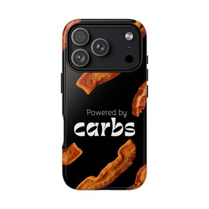 Könnte beinhalten: Schwarze Handyhülle mit einem Design mit knusprigen Speckstreifen auf schwarzem Hintergrund. Der Text "Powered by carbs" ist in weißer, fetter Schrift dargestellt. Die Hülle hat eine glänzende Oberfläche und einen Kameraausschnitt.