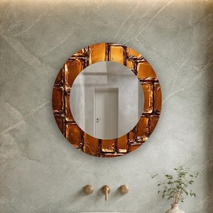 May include: A round wall mirror featuring a reflective center and a wide, textured frame with a glossy, deep amber-colored finish. The frame consists of numerous rectangular, block-like segments that create a layered, three-dimensional appearance.