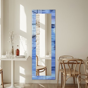 May include: A full-length mirror with a blue and white abstract design frame. The mirror is standing in a dining room setting with a white table and chairs.