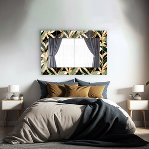 May include: A rectangular mirror with a decorative frame featuring a leaf pattern in gold, black, and green hangs above a bed. The bed has a beige duvet, blue pillows, and a dark blue throw. Two white bedside tables with lamps flank the bed.