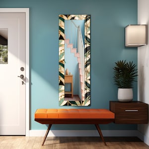 May include: A long, rectangular mirror with a patterned frame in black, green, gold, and white, reflecting a staircase. The mirror hangs on a teal wall above an orange bench with wooden legs. The room has a modern design.