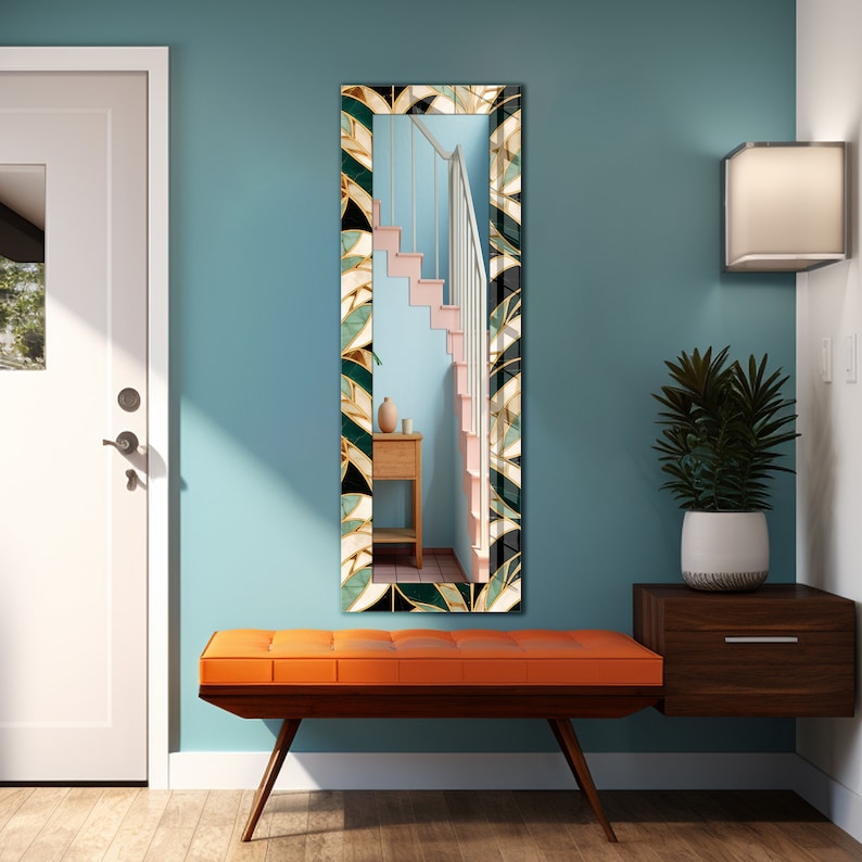 May include: A long, rectangular mirror with a patterned frame in black, green, gold, and white, reflecting a staircase. The mirror hangs on a teal wall above an orange bench with wooden legs. The room has a modern design.