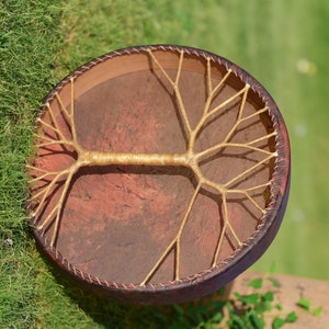 May include: A brown leather drum with a tree-like design made of woven rope. The drum is round and has a diameter of about 30 cm.