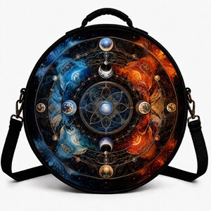 Puede incluir: Un bolso bandolera negro de forma circular con un estampado celestial vibrante. El diseño muestra un mandala central rodeado de fases lunares, con una paleta de colores azules a la izquierda y naranjas a la derecha, incluyendo un asa superior.
