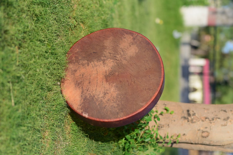 May include: A brown leather drum with a natural finish. The drum is sitting on a bed of green grass.