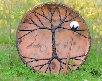 Può includere: Un tamburo in pelle marrone con un design ad albero della vita nero e una bacchetta bianca e nera.