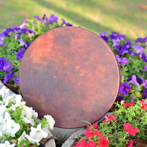 May include: A large, round, brown drum with a textured surface. The drum is surrounded by vibrant flowers in shades of purple, white, and red. The image is taken outdoors, with a natural background.