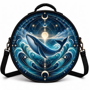 May include: A round black shoulder bag featuring a vibrant graphic print of a blue whale swimming through stylized ocean waves under a starry night sky with a central moon and celestial geometric lines, complete with a black handle and strap.