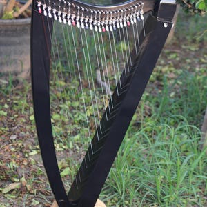 May include: A black harp with a wooden stand. The harp has strings and tuning pegs.