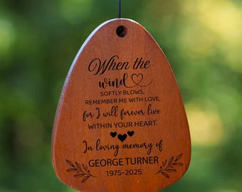 Könnte beinhalten: Ein Windspiel mit sechs schwarzen Metallröhren, die an einem runden Holzteil hängen. Ein hölzerner Windfänger ist mit folgendem Text graviert: When the wind softly blows, remember me with love, for I will forever live within your heart.