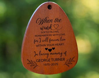 Könnte beinhalten: Ein Windspiel mit sechs schwarzen Metallröhren, die an einem runden Holzteil hängen. Ein hölzerner Windfänger ist mit folgendem Text graviert: When the wind softly blows, remember me with love, for I will forever live within your heart.