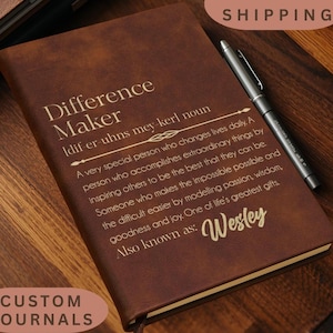 May include: A brown leather-like journal featuring the gold-printed text Difference Maker, a phonetic pronunciation, a definition of the term, and the name Wesley, accompanied by a silver metal pen resting on the cover of the closed notebook.