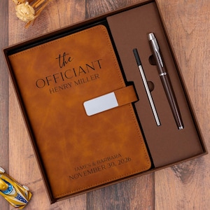 May include: A brown leather journal and pen set in a gift box. The journal is embossed with "the Officiant" and a name. The box also contains a pen and a pen refill. The date "November 30, 2026" is printed on the journal.