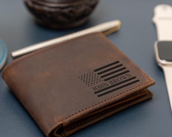 Könnte beinhalten: Ein braunes Leder-Brieftaschen-Modell mit einer lasergravierten amerikanischen Flagge auf der Vorderseite. Die Gravur enthält den Namen JOHN BROWN, der in die Streifen der Flagge integriert ist. Das Portemonnaie hat sichtbare Nähte und eine matte Oberfläche.