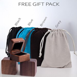 May include: A wooden ring box with an open lid sits in front of four drawstring bags in black, blue, brown, and grey. The bags have matching drawstrings. The text "FREE GIFT PACK" is at the top of the image.