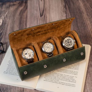 May include: A dark green cylindrical watch roll case with a tan suede interior, featuring three individual watch compartments. The interior lid is engraved with the text: Happy Birthday to the love of my life. My heart belongs to you.