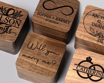 Könnte beinhalten: Fünf quadratische Holzschatullen mit dunkelbrauner Maserung, jede mit individuellen Lasergravuren versehen, darunter Texte wie Mr & Mrs Wilson, Sophia + Barney 07.06.2024, Rachel & Dean, Will you marry me? und Catherine mit Ringgrafiken.
