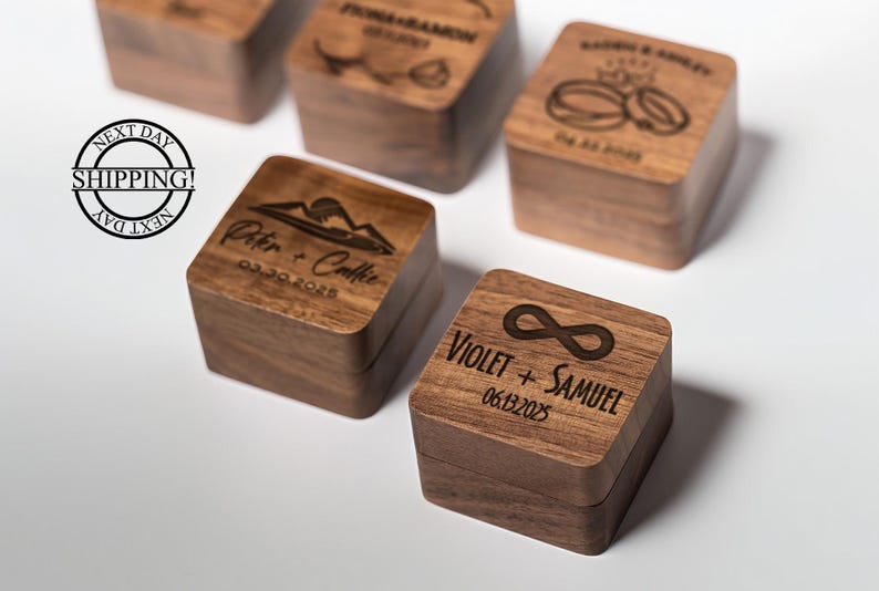 May include: A collection of wooden ring boxes, each with unique engraved details. One box displays an infinity symbol and the names "Violet + Samuel" with the date "06.13.2025". Other boxes feature names and dates.