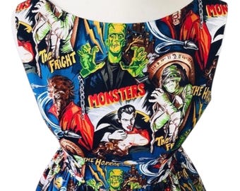 May include: A sleeveless dress featuring a vibrant all-over print of classic horror movie monsters including Frankenstein, a mummy, and a vampire. The blue fabric displays comic book style illustrations with text reading The Fright and Monsters.