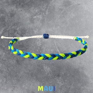 May include: Braided bracelet featuring a vibrant pattern of blue and neon yellow threads. The bracelet has a white adjustable cord and a dark blue knot. The word "MAUI" is displayed in neon yellow and blue.