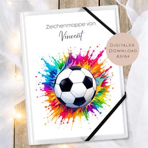 May include: White notebook with a soccer ball design. The soccer ball is black and white, set against a vibrant splash of rainbow colors. The text "Zeichenmappe von Vincent" is at the top. A black elastic band secures the notebook.