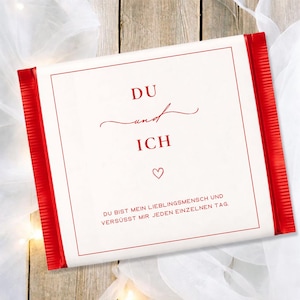 May include: A white rectangular gift with red edges and a red border. The text "DU und ICH" is printed in red script, along with a heart symbol. The bottom of the gift has additional text.