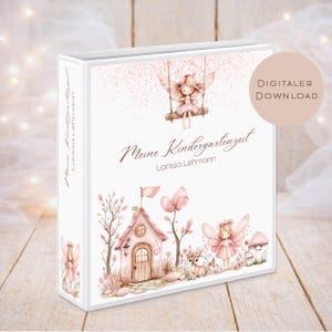 Puede incluir: Una carpeta blanca con un diseño caprichoso que presenta un hada en un columpio, una casa de hadas y el texto "Meine Kindergartenzeit" de Larissa Lehmann. La portada está adornada con ilustraciones en rosa y marrón.