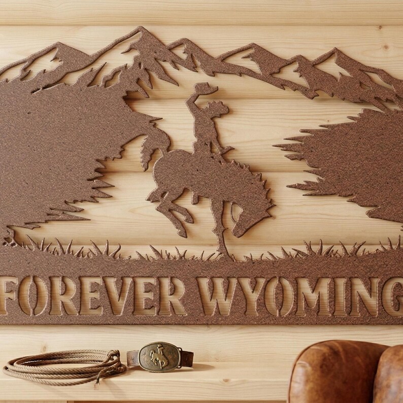 May include: A brown metal wall art piece featuring a silhouette of a cowboy riding a bucking horse against a mountain range, with the text FOREVER WYOMING below. Included are a coiled rope and a metal belt buckle with a bucking horse design.