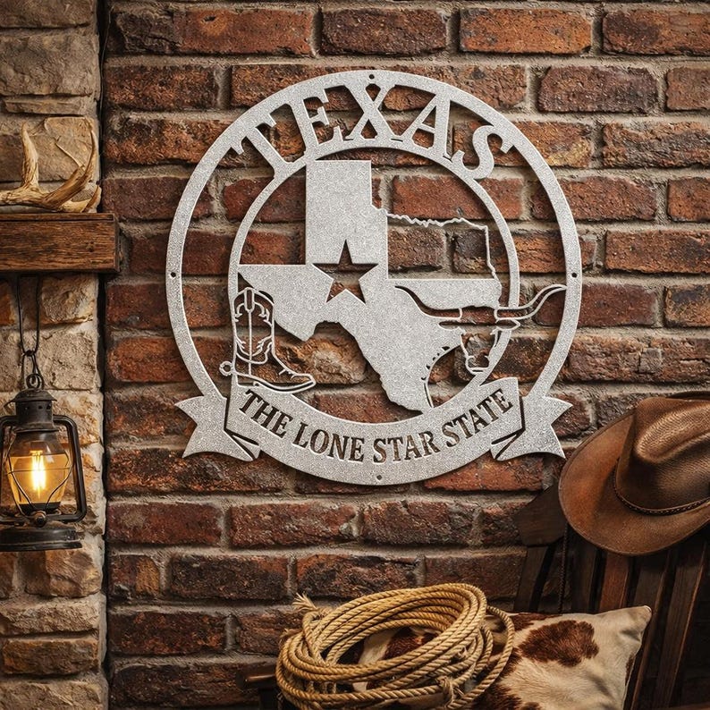 Pu&ograve; includere: Un'opera d'arte da parete in metallo argentato raffigurante lo stato del Texas, una stella, uno stivale da cowboy e un longhorn. Il testo "TEXAS" &egrave; in alto e "THE LONE STAR STATE" in basso. Montato su un muro di mattoni.