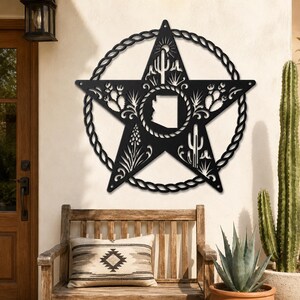 May include: A black metal wall art piece shaped like a five-pointed star enclosed in a rope-style circular frame. The star features cutouts of the state of Arizona in the center, surrounded by desert flora including cacti and sun motifs.