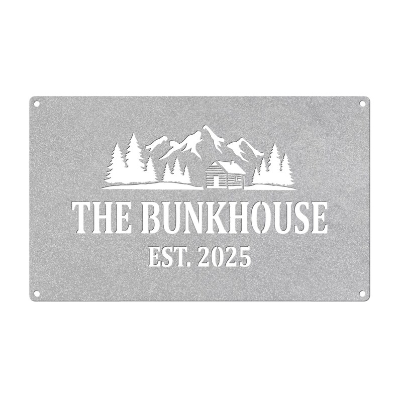 May include: A rectangular, silver-colored metal sign with the words "THE BUNKHOUSE" and "EST. 2025" cut out in a bold font. Above the text is a mountain and cabin scene, also cut out. Four small holes are in each corner.